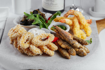 fried fish with sauce and greens with squid rings, mussels and shrimp on a white paper