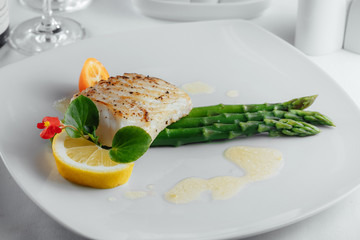 fish with a slice of lemon and asparagus on a white plate