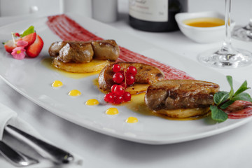 meat on potato slices with currant and sauce on a white plate