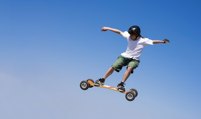 Naklejka na ściany i meble Skateboarder doing a jumping trick at skateboard park with mountainboard