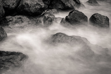 Obraz na płótnie Canvas motion blur water surrounding rocks, black and white