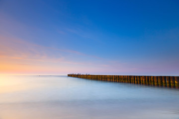 Fototapeta na wymiar sunset on the beach with a wooden breakwater, long exposure
