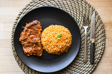 Steak with tomato sauce and bulgur rice in a black plate