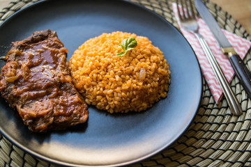 Steak with tomato sauce and bulgur rice in a black plate