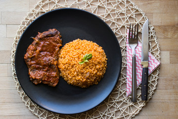 Steak with tomato sauce and bulgur rice in a black plate