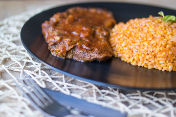 Steak with tomato sauce and bulgur rice in a black plate