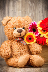Beautiful flowers and a teddy bear on wooden background