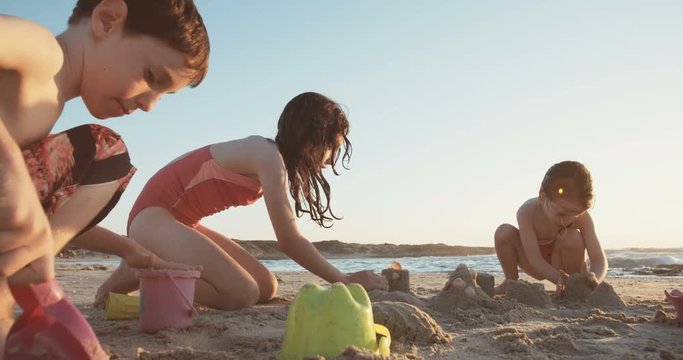 Three kids building sand castles on the beach during sunset