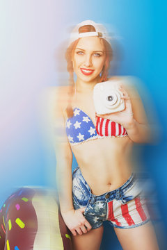 Young woman in American flag shorts and bikini top with instant camera
