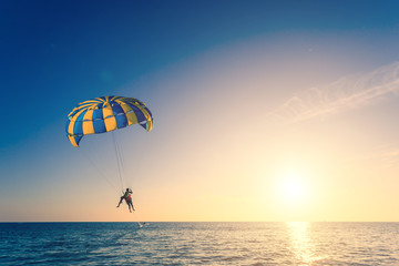 Tourist is para sailing over the blue se. Lens flare and warm to