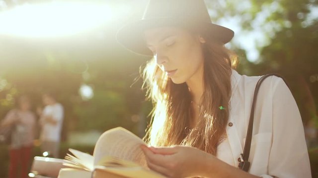 Young beautiful girl in hat reading book in city park. Slow motion.