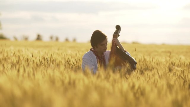 Young man playing pandora in wheat field at sunset.