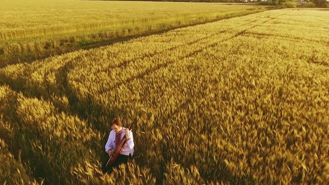 Young man playing pandora in wheat field at sunset. Slow motion. Aerial view.