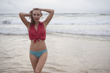 Beautiful blonde happy woman wearing red collar shirt and blue bikini bottom posing on a beautiful summer day at the beach over sea and sky background
