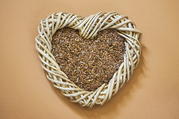 Flax seed in woven heart-shaped basket on light brown background. Copy space