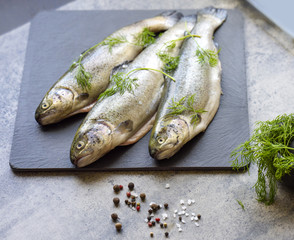 Rainbow trouts on a stone board with herbs and mortar
