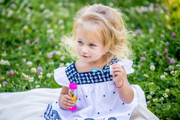 Little girls blow bubbles sitting on the grass