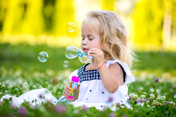 Little girls blow bubbles sitting on the grass