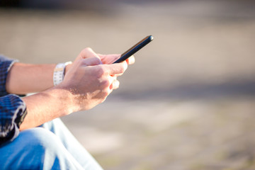 Closeup of male hands is holding cellphone outdoors on the street. Man using mobile smartphone.