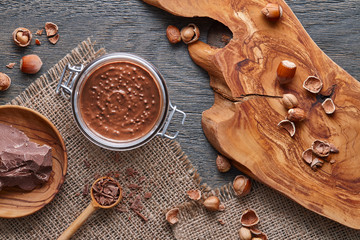 Glass jar of hazelnut spread on wooden background