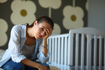 Young tired woman sitting on the bed near children's cot.