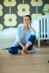 Young woman sitting on the floor near children's cot.