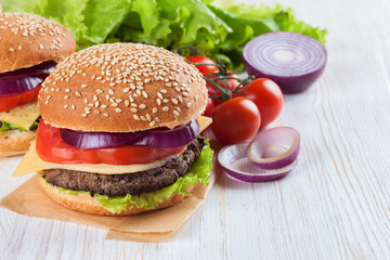 Homemade cheeseburger on white wooden surface.
