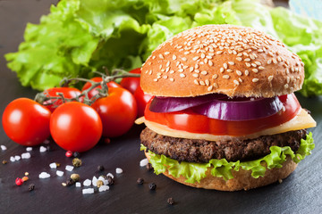 Homemade cheeseburger on black slate surface.
