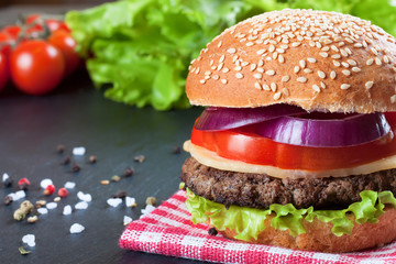 Homemade cheeseburger on black slate surface.