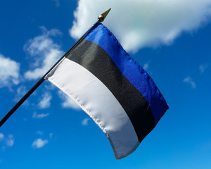 Estonian flag held up against a blue sky with a few clouds. - 116504782