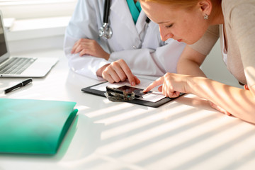 Doctor pointing into medical history form and discussing something with her patient. Close-up.