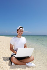 美しいビーチでパソコンを楽しむ笑顔の男性
