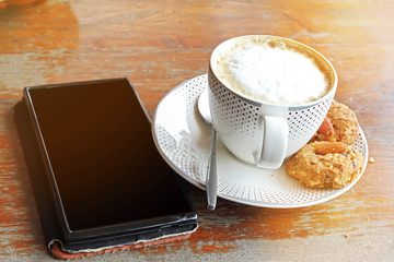 Coffee cup of cappuccino and cookie .effect vintage style blur and noise.relax with coffee and cookie and smart phone