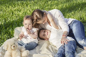 Young Caucasian mother with her son and a toddler daughter playing on the grass on a bright summer day