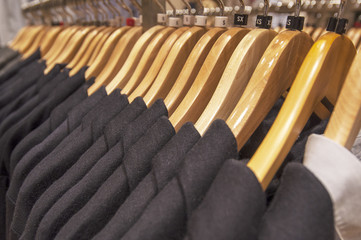 Obraz premium Clothes hang on a shelf in a clothes shopping center . Black coat or suit for winter or autumn season