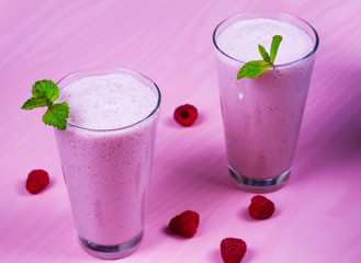 Raspberry milkshake garnished with mint on pink wooden background