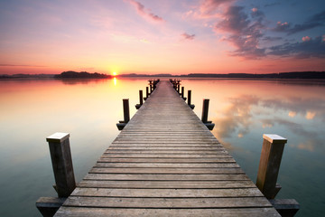 Fototapeta na wymiar langer Holzsteg am Seeufer zum Sonnenaufgang im Sommer