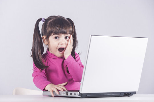 Cute little girl reacts with shock while using a laptop. Internet safety concept