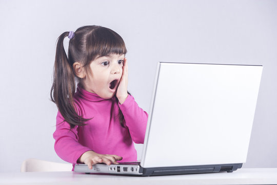 Cute little girl reacts with shock while using a laptop. Internet safety concept