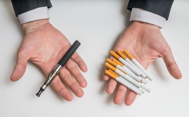 Hands are holding electronic and conventional tobacco cigarettes and comparing them