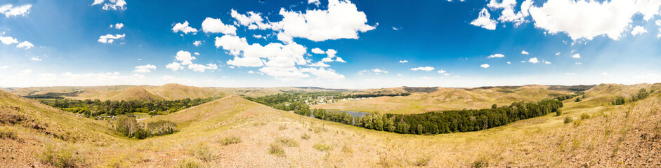 Summer panorama of the hilly terrain of the steppe lake, trees and village.