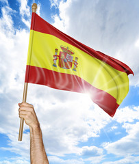 Person's hand holding the Spanish national flag and waving it in the sky, 3D rendering