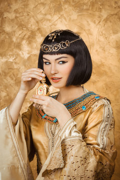 Beautiful Egyptian Woman Like Cleopatra With Perfume Bottle On Golden Background