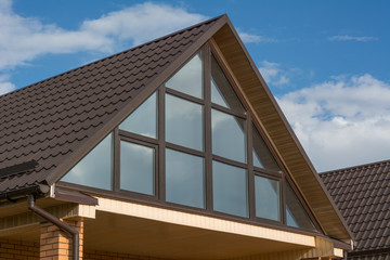 Attic panoramic window under the roof reflects clouds sky