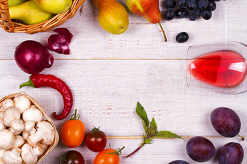 Grape, apples, pears, mushrooms, chili peppers, tomatoes, basil, red onions and glass of red wine on a white wooden background. View from above, top studio shot of vegetables and fruits