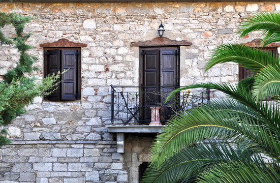 Window and door on the balcony of the house made ​​of stone with palm tree in a mediterranean village.