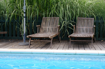 Two wooden sun loungers by the side of a swimming pool