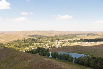 Fototapeta na wymiar Summer panorama of the hilly terrain of the steppe lake, trees and village.