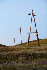 Fototapeta na wymiar The old crooked poles of power lines on the steppe hills.