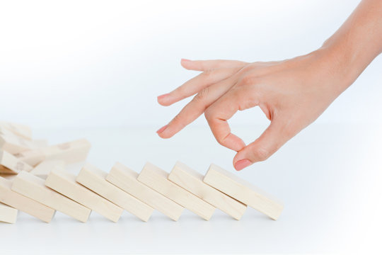 Human hand starting a domino effect concept with wooden blocks